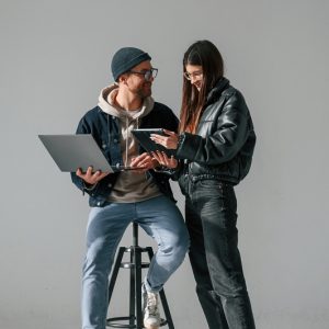 Beautiful man and woman are together in the studio against background. With laptop and tablet in hands.